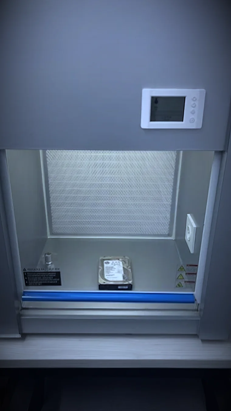 Interior de la cabina de flujo laminar de RDC: el filtro HEPA al fondo, un disco duro sobre la superficie de trabajo y el panel de control